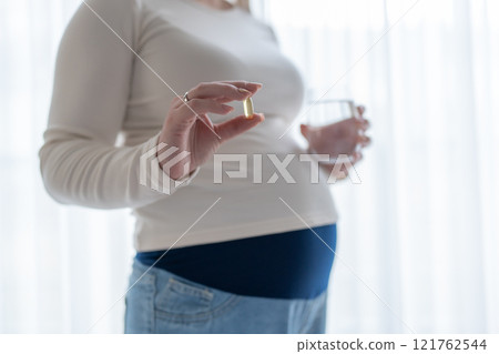 Pregnant woman holding a glass of water and taking vitamins during pregnancy. Pregnancy, health, pharmaceuticals, care. Close up Pregnant woman holding a glass of water and taking vitamins during pregnancy. Pregnancy, health, pharmaceuticals, care. Close up 121762544