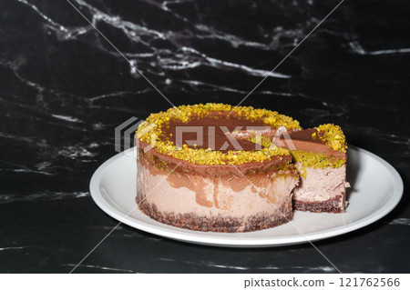 Sliced chocolate Dubai cheesecake with pistachio paste and kataifi dough filling covered in chocolate ganache on white plate. Black background copy space. Indulgence, gourmet desserts, art of culinary Sliced chocolate Dubai cheesecake with pistachio paste and kataifi dough filling covered in chocolate ganache on white plate. Black background copy space. Indulgence, gourmet desserts, art of culinary 121762566
