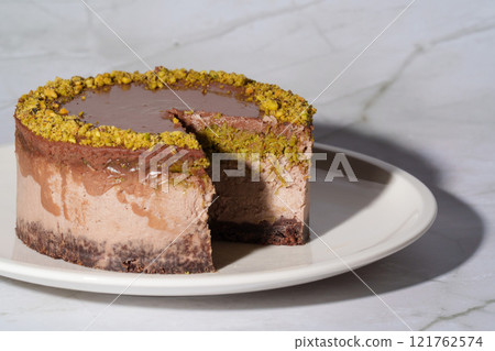 Dubai chocolate cheesecake with pistachio paste and kataifi dough covered in chocolate ganache on a white plate. White background with copy space. Indulgence, gourmet desserts, art of culinary 121762574
