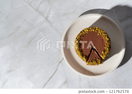 Top view of Dubai chocolate cheesecake with pistachio paste and kataifi covered in chocolate ganache on white plate. White background with copy space. Indulgence, gourmet desserts, art of culinary Top view of Dubai chocolate cheesecake with pistachio paste and kataifi covered in chocolate ganache on white plate. White background with copy space. Indulgence, gourmet desserts, art of culinary 121762578