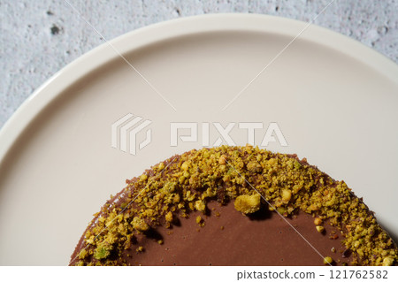 Close up of Dubai chocolate cheesecake decoration with pistachio and kataifi dough covered in chocolate ganache on white plate. Gray background copy space.Indulgence, gourmet desserts, art of culinary Close up of Dubai chocolate cheesecake decoration with pistachio and kataifi dough covered in chocolate ganache on white plate. Gray background copy space.Indulgence, gourmet desserts, art of culinary 121762582
