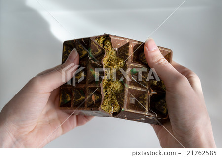 Dubai chocolate with pistachio, tahini and kadaif, chocolate broken in woman's hands Dubai chocolate with pistachio, tahini and kadaif, chocolate broken in woman's hands 121762585