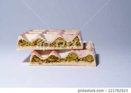 Popular white Dubai chocolate with pistachio, dried raspberry, tahini and kadaif, on white background, isolated, showing the filling. Confectionery and handmade sweets, chocolatier Popular white Dubai chocolate with pistachio, dried raspberry, tahini and kadaif, on white background, isolated, showing the filling. Confectionery and handmade sweets, chocolatier 121762823