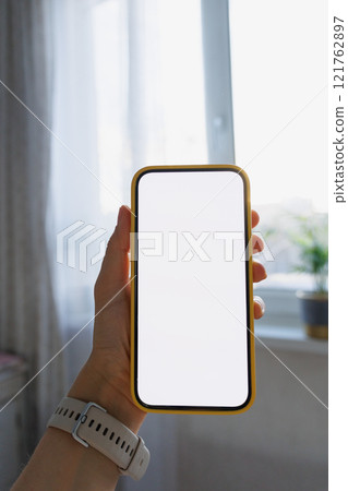 Close-up of human hand holding black white-screen mobile phone in interior background. mockup Close-up of human hand holding black white-screen mobile phone in interior background. mockup 121762897