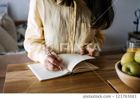 Close-up of a woman journaling at a wooden table with fresh apples. The art of journaling for mindfulness, self-reflection, and personal growth. Close-up of a woman journaling at a wooden table with fresh apples. The art of journaling for mindfulness, self-reflection, and personal growth. 121763081