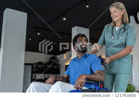 Mature female doctor carrying a wheeling-chair with a male patient Mature female doctor carrying a wheeling-chair with a male patient 121763088