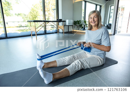 Woman stretching with resistance band during physiotherapy treatment for leg injury 121763106