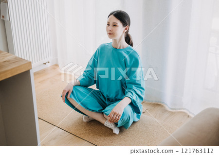 Woman meditating indoors in natural light, seated cross-legged on a yoga mat, focusing on calmness and mindful movement for holistic health. Woman meditating indoors in natural light, seated cross-legged on a yoga mat, focusing on calmness and mindful movement for holistic health. 121763112