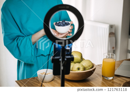 Woman presenting fresh blueberries with a ring light setup. Content creation at home, vlogging essentials, and personal branding tools. Woman presenting fresh blueberries with a ring light setup. Content creation at home, vlogging essentials, and personal branding tools. 121763118