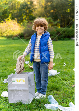 Small male child collecting trash outdoors in volunteers project sorting waste 121763168