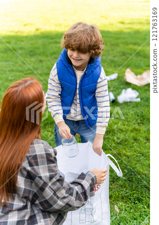Care for nature. Female teacher guiding little boy collecting trash in park 121763169