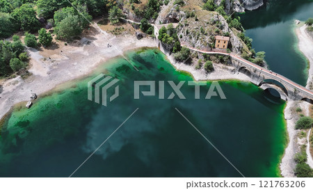 Tourists crossing bridge over vivid green lake in italy Tourists crossing bridge over vivid green lake in italy 121763206