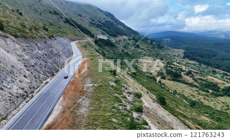 Car driving on empty mountain road under cloudy sky Car driving on empty mountain road under cloudy sky 121763243