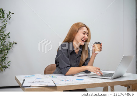 Young Female Accountant Working on Financial Accounting Tasks with Laptop and Coffee in Modern Office Setting 121764069