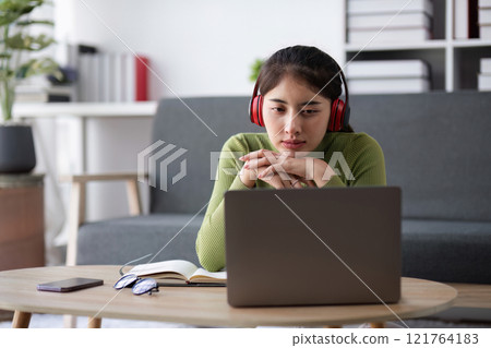 Young Woman Feeling Stressed While Working Online from Home, Wearing Headphones and Using Laptop in Modern Living Room Young Woman Feeling Stressed While Working Online from Home, Wearing Headphones and Using Laptop in Modern Living Room 121764183