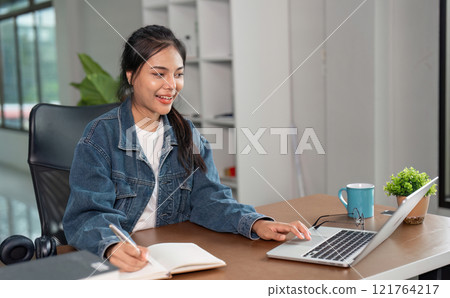 Young Woman Studying Online at Home with Laptop and Notebook, Engaged in E-Learning and Remote Education in a Modern Workspace 121764217