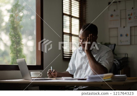 Exhausted American Businessman Working Long Hours at Home Office Desk with Laptop and Coffee 121764323
