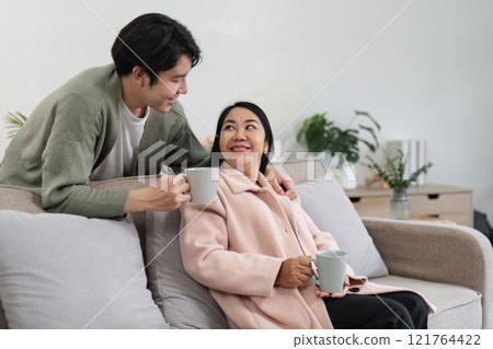 Mother and Son Relaxing in a Cozy Modern Living Room, Enjoying Quality Time Together with Warm Beverages Mother and Son Relaxing in a Cozy Modern Living Room, Enjoying Quality Time Together with Warm Beverages 121764422