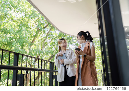 Professional Business Women Engaged in a Collaborative Discussion Outdoors with Modern Technology and Natural Background 121764466
