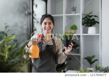 Young Woman Creating a Cozy Indoor Garden with Houseplants in a Modern Room Setting Young Woman Creating a Cozy Indoor Garden with Houseplants in a Modern Room Setting 121764677
