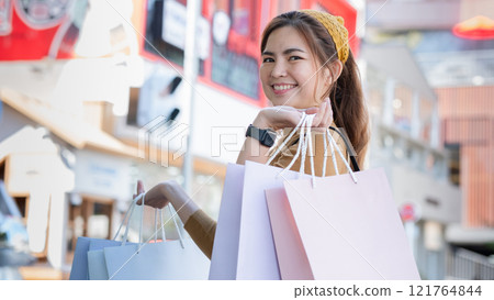 Young Woman Enjoying a Day of Shopping with Multiple Bags in Urban Setting, Smiling and Fashionably Dressed, Reflecting Modern Lifestyle Young Woman Enjoying a Day of Shopping with Multiple Bags in Urban Setting, Smiling and Fashionably Dressed, Reflecting Modern Lifestyle 121764844