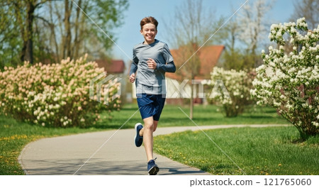 Caucasian teen boy running in spring park for fitness and wellbeing 121765060