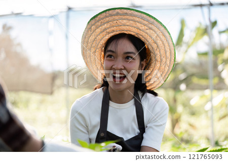 Cheerful Female Farmer Smiling in Sunlit Greenhouse with Straw Hat and Apron, Embracing Sustainable Agriculture and Organic Farming Cheerful Female Farmer Smiling in Sunlit Greenhouse with Straw Hat and Apron, Embracing Sustainable Agriculture and Organic Farming 121765093