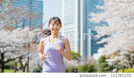 Urban fitness: young asian female jogging amidst cherry blossoms and city skyline 121765270
