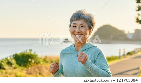 Energetic elderly asian female enjoying a morning jog by the beach with natural scenery 121765384