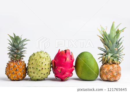 Exotic fresh summer fruits on white background. Dragon fruit, pineapple, persimmon, mango, annona cherimola flat lay with free copy space. 121765645