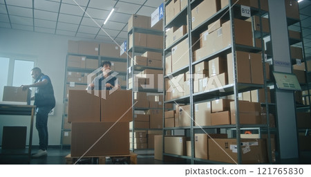 Male inventory manager pushes pallet truck with cardboard boxes in warehouse, scans code on parcel Male inventory manager pushes pallet truck with cardboard boxes in warehouse, scans code on parcel 121765830