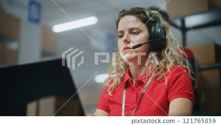 Female logistics coordinator in headset talks with customer, uses laptop 121765859