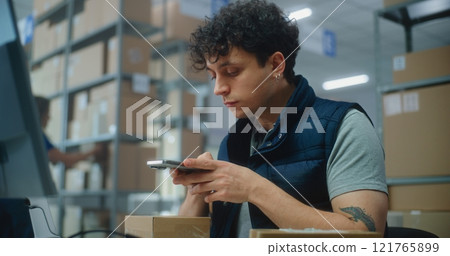 Logistics manager scans small parcels using smartphone, works in warehouse of post office Logistics manager scans small parcels using smartphone, works in warehouse of post office 121765899