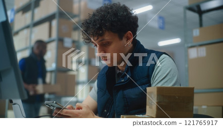 Logistics manager scans small parcels using smartphone, works in warehouse of post office Logistics manager scans small parcels using smartphone, works in warehouse of post office 121765917
