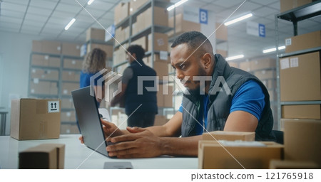 African American post office employee scans parcels with barcode scanner, enters data on laptop African American post office employee scans parcels with barcode scanner, enters data on laptop 121765918