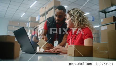 Team of multiethnic warehouse associates scan cardboard box, check information on laptop 121765924