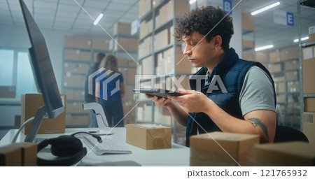 Male warehouse clerk scans parcels for delivery using tablet, works in store logistics storage 121765932