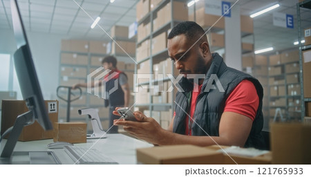 African American logistics manager scans parcels using smartphone, works in warehouse 121765933