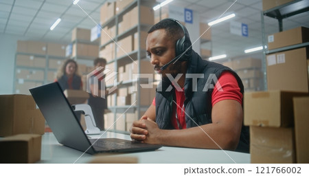 Portrait of African American logistics coordinator in headset talking to client, looking at camera 121766002