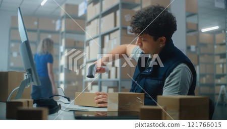 Male inventory manager works on computer, scans parcels, prepares package for shipping 121766015