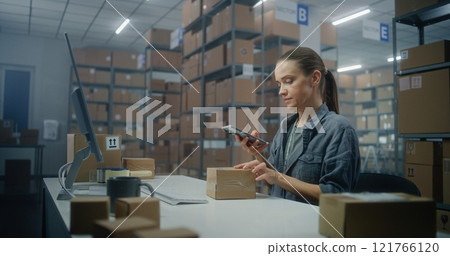 Female logistics manager scans parcel using smartphone, enters information on computer 121766120