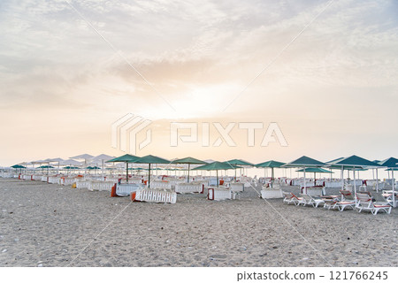 Lot of white deck chairs under an umbrella on a clean beach at sunset or sunrise. 121766245