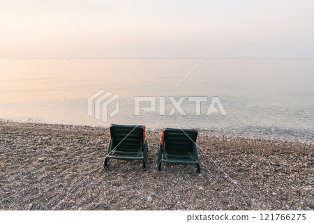 Plastic sun beds with orange capes on the sea beach at sunrise. Summer vacation concept. Plastic sun beds with orange capes on the sea beach at sunrise. Summer vacation concept. 121766275