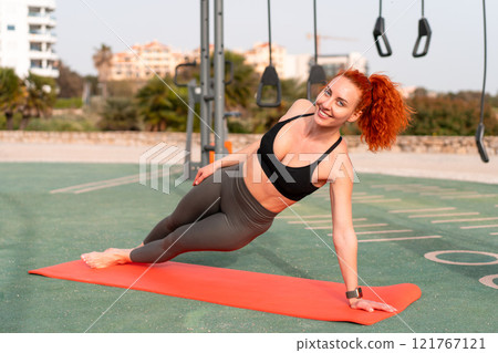 Happy sporty woman practicing side plank on mat at Happy sporty woman practicing side plank on mat at 121767121