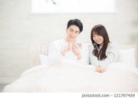 A newlywed couple relaxing in a beautiful bedroom looking at their smartphones 121767489