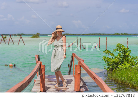 Female tourist in a turquoise dress standing on a wooden pier over the turquoise waters of Bacalar Lake, Mexico. Peaceful tropical travel destination concept Female tourist in a turquoise dress standing on a wooden pier over the turquoise waters of Bacalar Lake, Mexico. Peaceful tropical travel destination concept 121767818