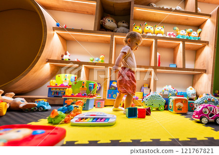 Toddler enjoying a playful and creative indoor environment filled with toys, games, and engaging activities for learning and fun Toddler enjoying a playful and creative indoor environment filled with toys, games, and engaging activities for learning and fun 121767821