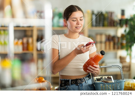 European young woman customer at shop scans QR code on grapefruit juice bottle using phone camera European young woman customer at shop scans QR code on grapefruit juice bottle using phone camera 121768024