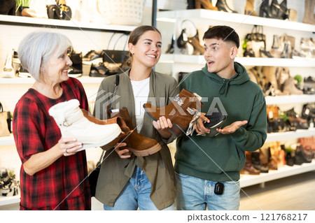 Mature woman sales consultant helps couple customers decide on choice of model of winter shoes Mature woman sales consultant helps couple customers decide on choice of model of winter shoes 121768217