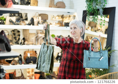 Elderly woman inspects shop window and is looking for modern, fashionable and roomy handbag 121768226
